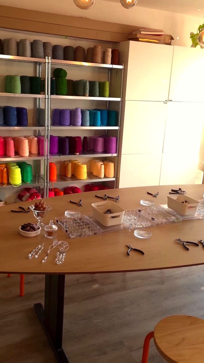 Sfeervol atelier met een grote werktafel en een kleurrijke wand vol garen