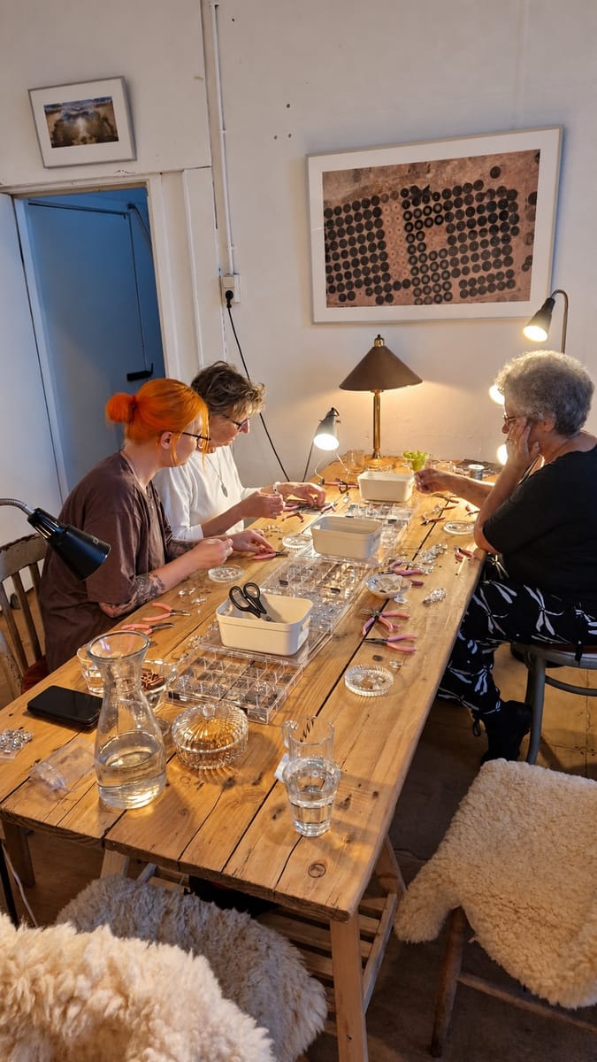 Drie deelnemers werken geconcentreerd aan hun eigen suncatchers aan de grote werktafel