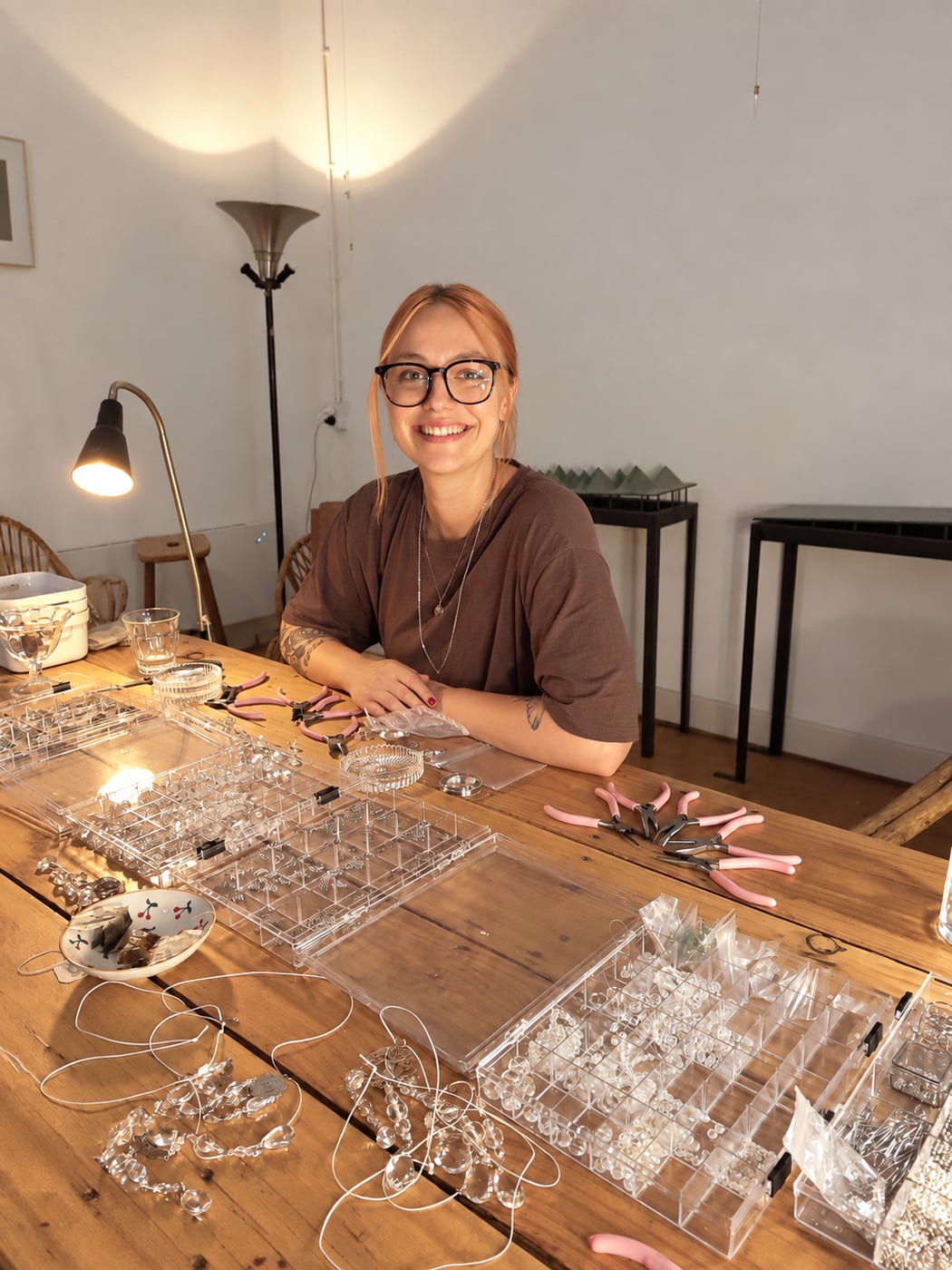 Kiki van Glistening Studio lachend aan haar werktafel vol kristallen en sieradengereedschap