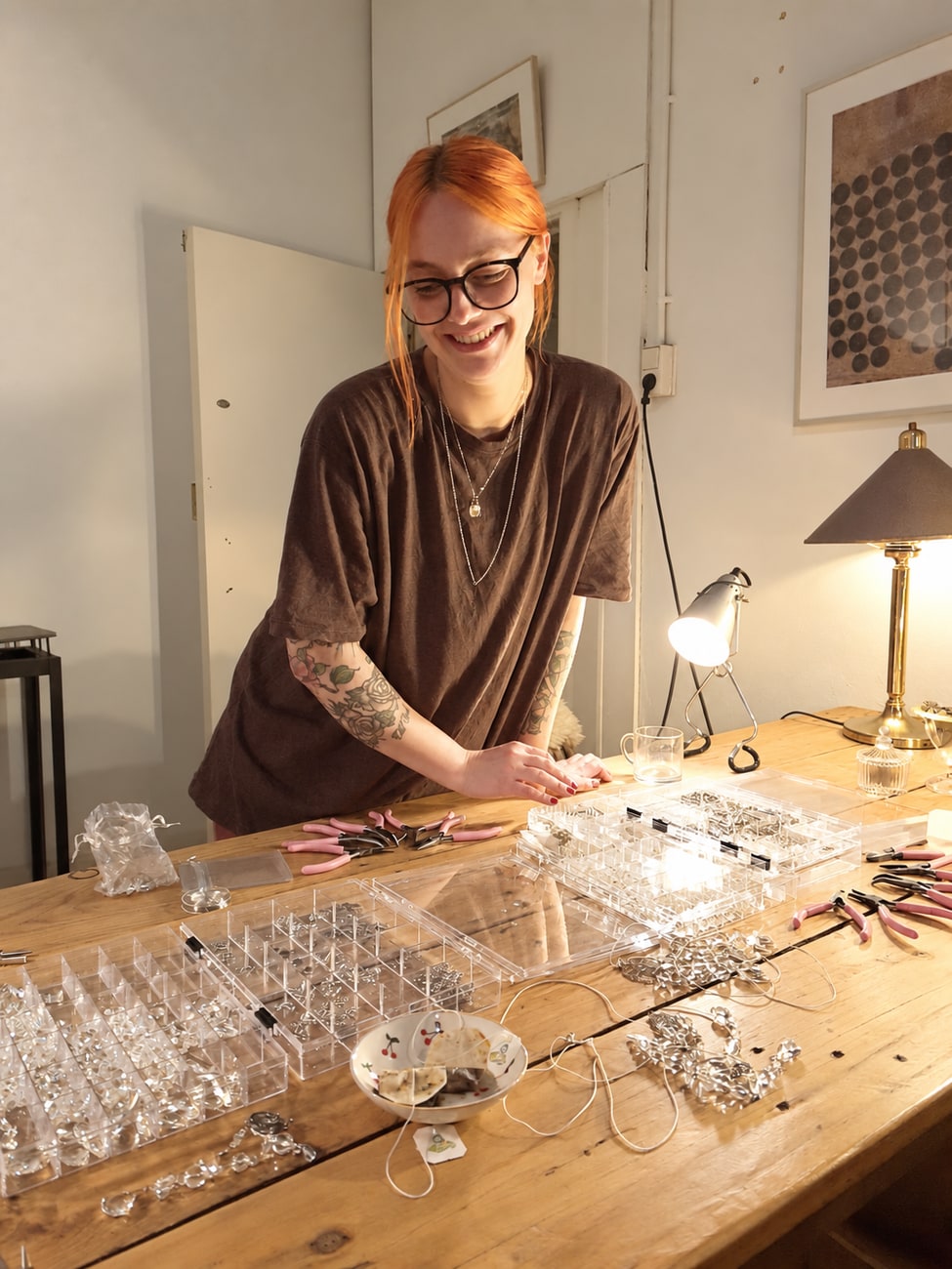 Kiki lacht terwijl ze aan haar werktafel kristallen en kralen sorteert voor het maken van suncatchers